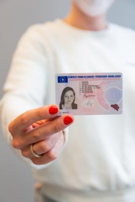 Dame met witte trui die een rijbewijs toont